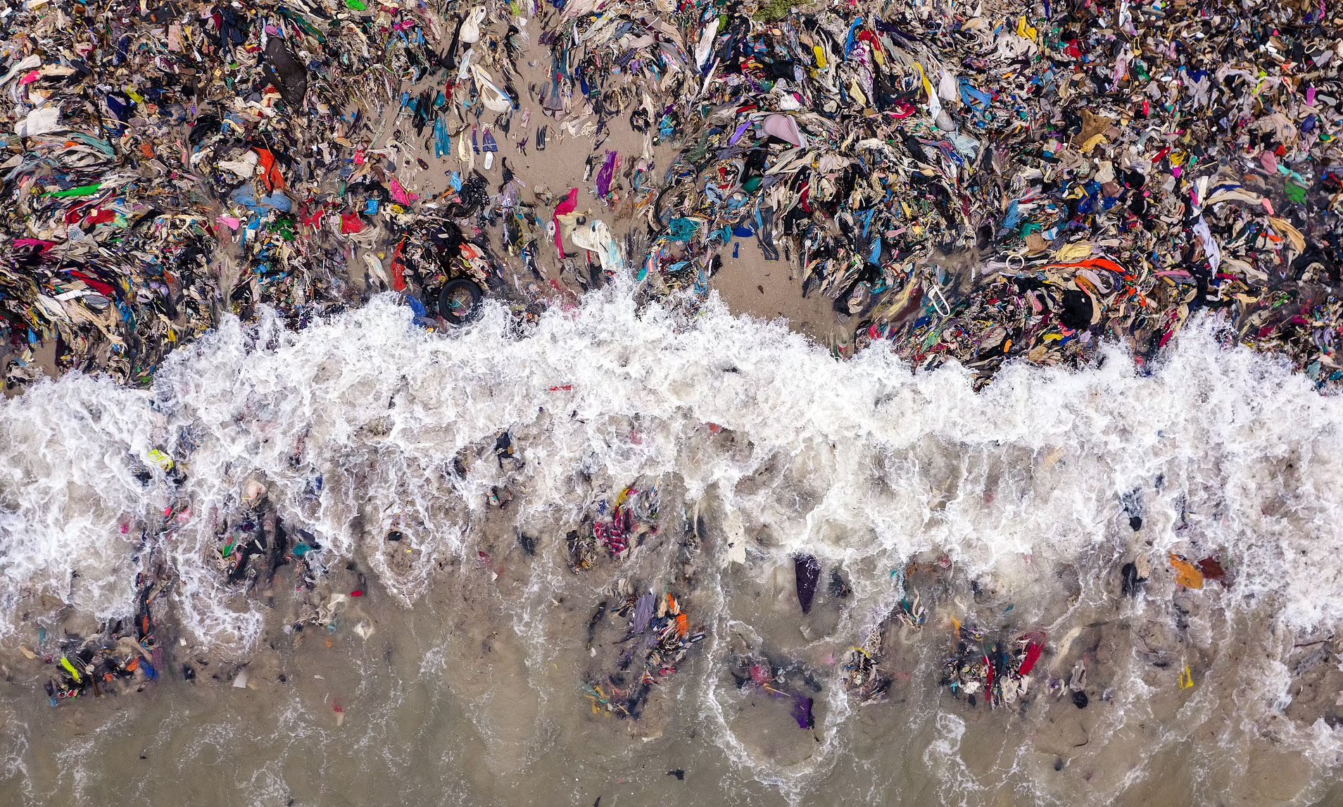 Des vêtements jetés polluent une rive, illustrant l’impact environnemental de la fast fashion.